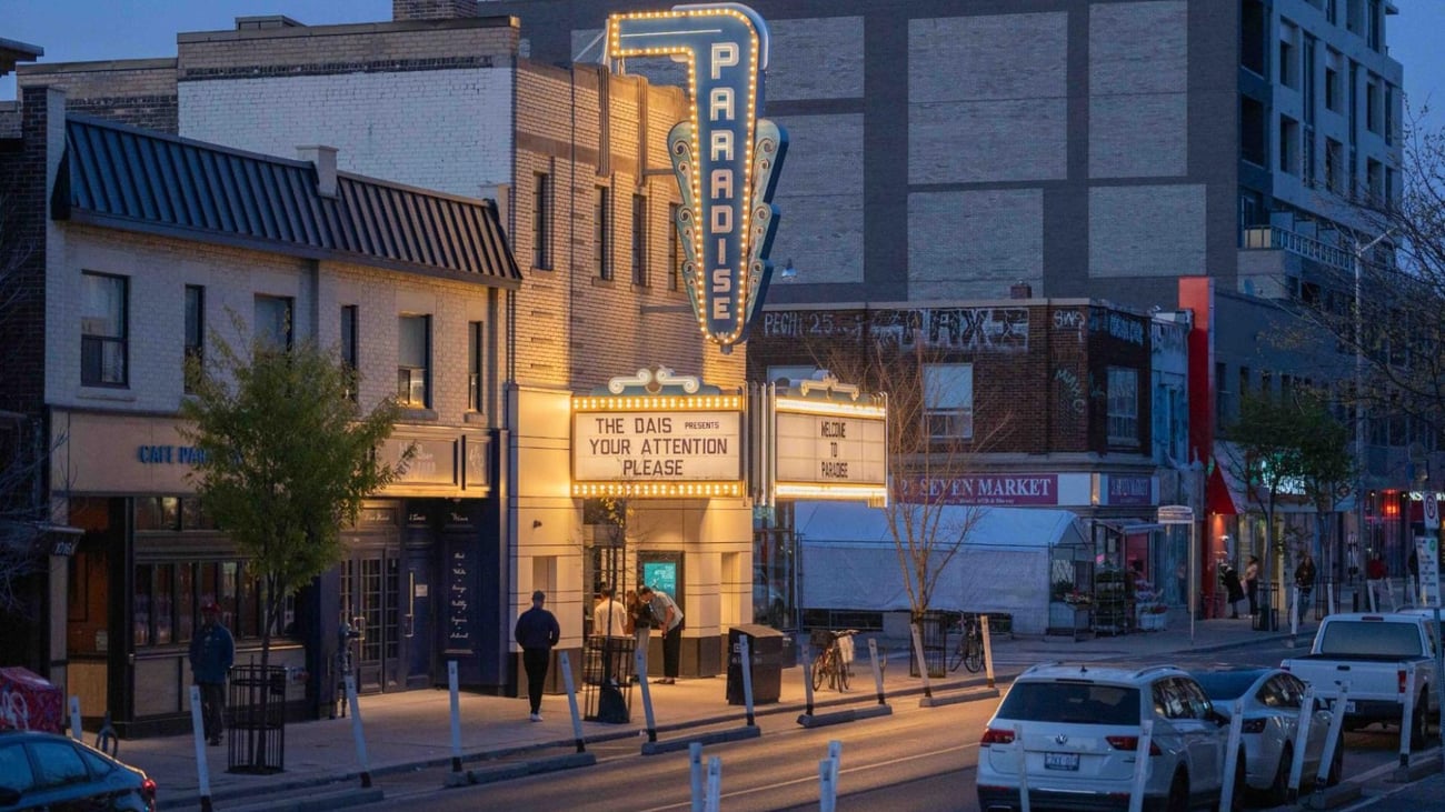 A small group of people at the box office of the Paradise Theatre, with the sign "The Dais presents YOUR ATTENTION PLEASE" A small group of people at the box office of the Paradise Theatre, with the sign "The Dais presents YOUR ATTENTION PLEASE"